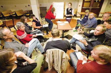 Group of adults seated in a circle in conversation, with one person taking notes on a flipchart.