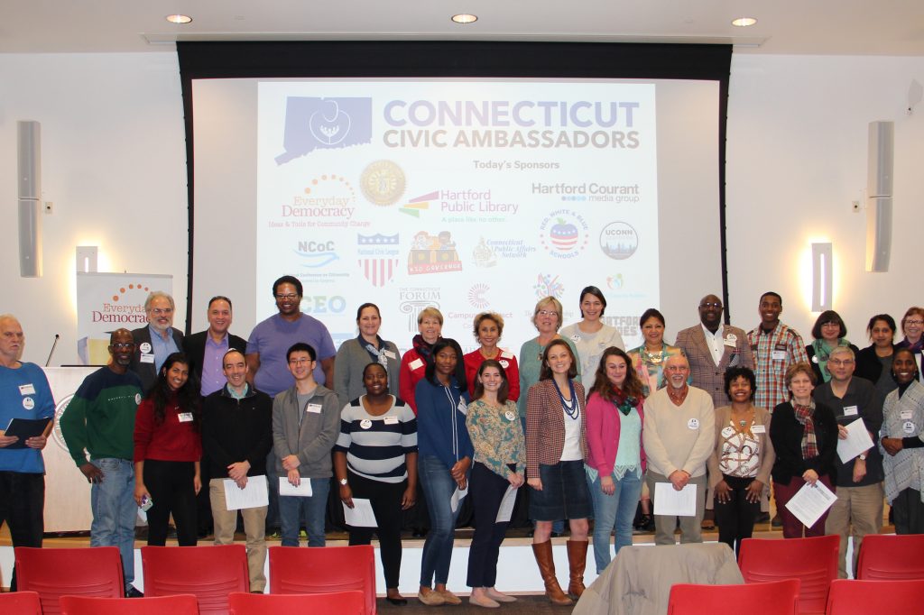 Group photo of smiling adults in front of a projector screen that says "Connecticut Civic Ambassadors"